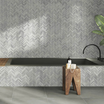 Des carreaux de pierre grise forment un mur à chevrons au-dessus d'une baignoire, complété par des tabourets en bois et une plan