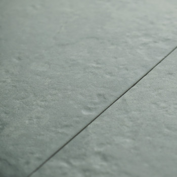 Un carreau gris-vert légèrement texturé est rejoint par une fine ligne de coulis sombre, posée selon un motif de sol intérieur h