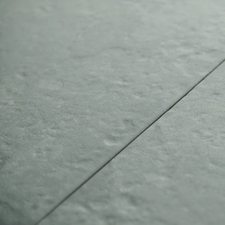 Un carreau gris-vert légèrement texturé est rejoint par une fine ligne de coulis sombre, posée selon un motif de sol intérieur h