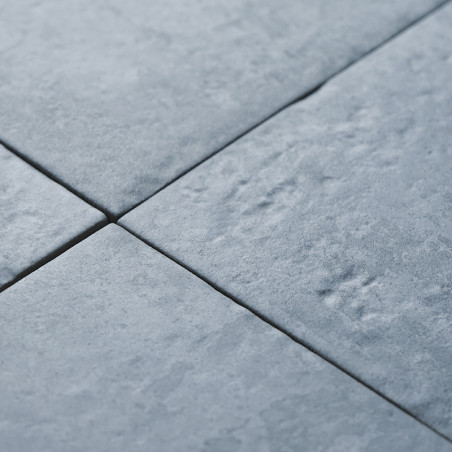 Cuatro azulejos grises, parecidos a la piedra, forman un patrón con texturas sutiles y ligeras hendiduras, creando una superfici