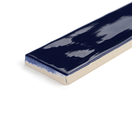 Un carreau de céramique rectangulaire présente un vernis bleu foncé brillant sur le dessus, avec des bords non vernis révélant u