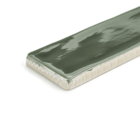 Un carreau de céramique rectangulaire, brillant et vert, reflète la lumière sur sa surface lisse. ses bords révèlent un dessous 