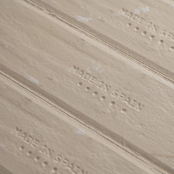 Op de getextureerde beige tegel staat `MADE IN SPAIN` in reliëfletters, omgeven door subtiele strepen en spikkels, wat een rusti