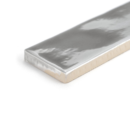 Eine rechteckige Keramikfliese weist ein glänzendes Silbermetallic-Finish auf und ruht auf einer schlichten weißen Oberfläche. S