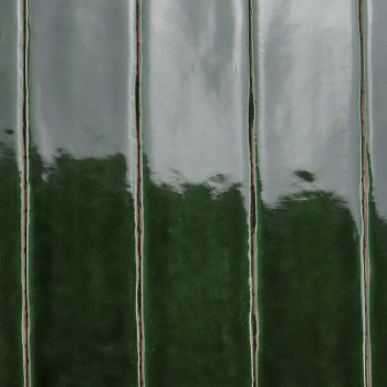 Ladrilhos cerâmicos verdes brilhantes ficam verticalmente, refletindo a luz. A alternância de tons claros e escuros cria uma apa