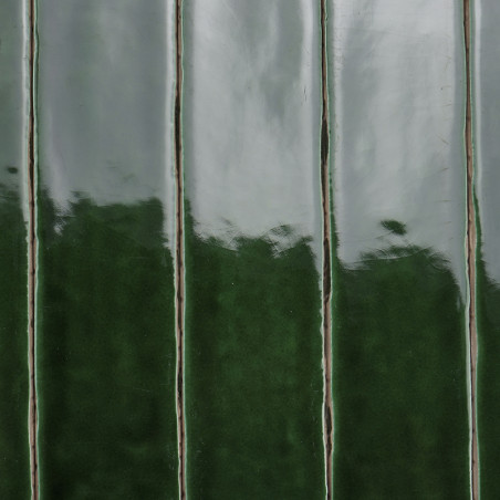 Glänzend grüne Keramikfliesen stehen vertikal und reflektieren das Licht. Die abwechselnden hellen und dunklen Farbtöne erzeugen