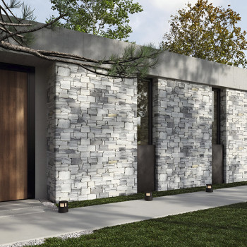 Des carreaux muraux en pierre recouvrent l'extérieur d'un bâtiment moderne, entouré d'une allée en béton et d'une pelouse verte.