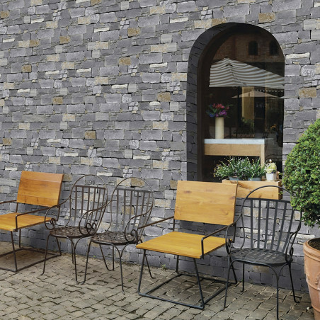 Steinfliesen bilden eine rustikale Wand, die ein großes Bogenfenster umrahmt, gesäumt von Eisenstühlen und Topfpflanzen auf eine