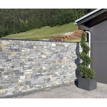 Stenen muur midden in een tuin, omzoomd door weelderig gras en bomen, grenzend aan de hoek van een modern gebouw.