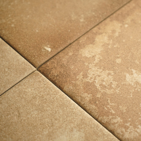 Quatre carreaux carrés texturés se croisent, présentant des tons brun terreux et des variations subtiles. Ils forment un quadril