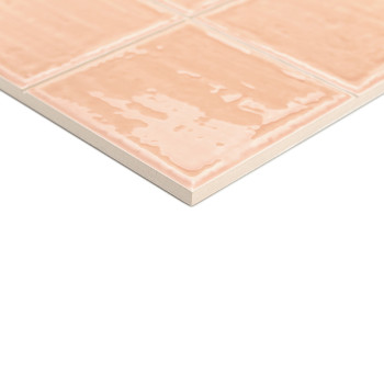 Un carreau de céramique au fini brillant de couleur pêche affiche un motif quadrillé, posé sur une surface blanche, suggérant un