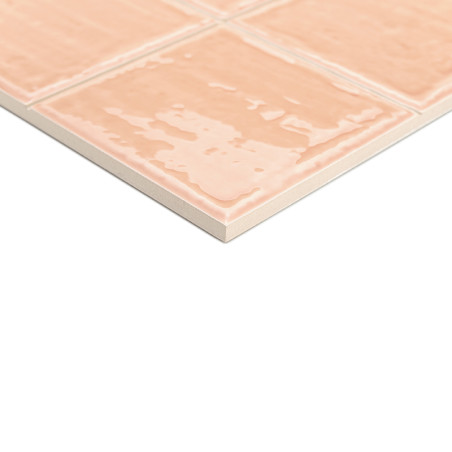 Un carreau de céramique au fini brillant de couleur pêche affiche un motif quadrillé, posé sur une surface blanche, suggérant un