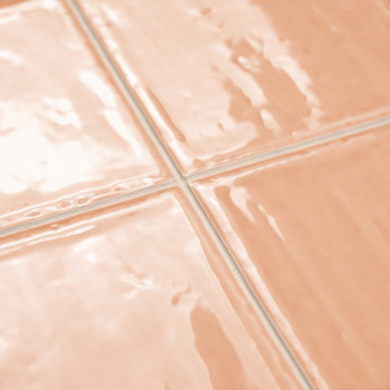 Quatre carreaux de céramique brillants de couleur pêche disposés dans une grille soignée reflètent la lumière. Le coulis entre e