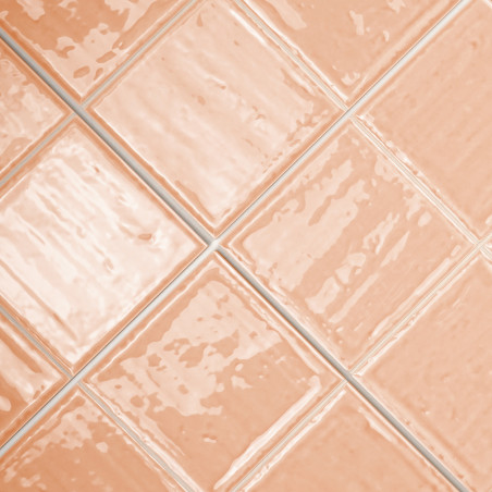 Vierkante, glanzende zalmkleurige tegels vormen een diagonaal patroon. hun gladde oppervlakken reflecteren licht, waardoor een g