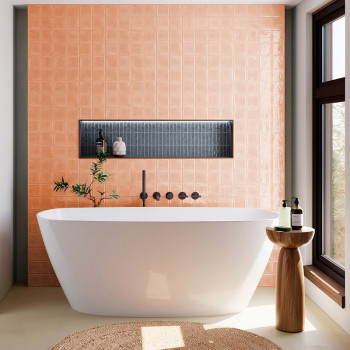 Une baignoire autoportante blanche repose contre un mur carrelé pêche avec une étagère noire encastrée avec décor, dans une sall