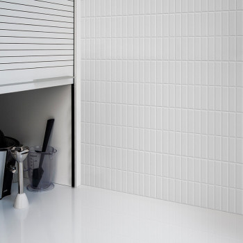 Ladrilhos brancos e verticais do metrô cobrem uma parede, refletindo a luz em uma cozinha elegante e moderna com armários e um b
