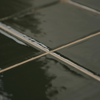 Glanzende groene keramische tegels vormen een gerasterd patroon en reflecteren licht. Ze zijn netjes uitgelijnd en creëren een g