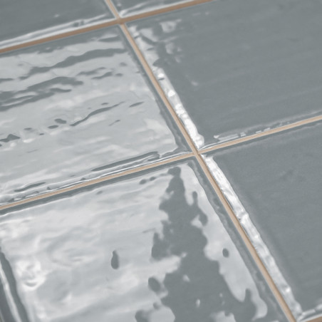 Les carreaux de céramique gris brillant sont disposés selon un motif en grille, réfléchissant la lumière pour révéler une textur