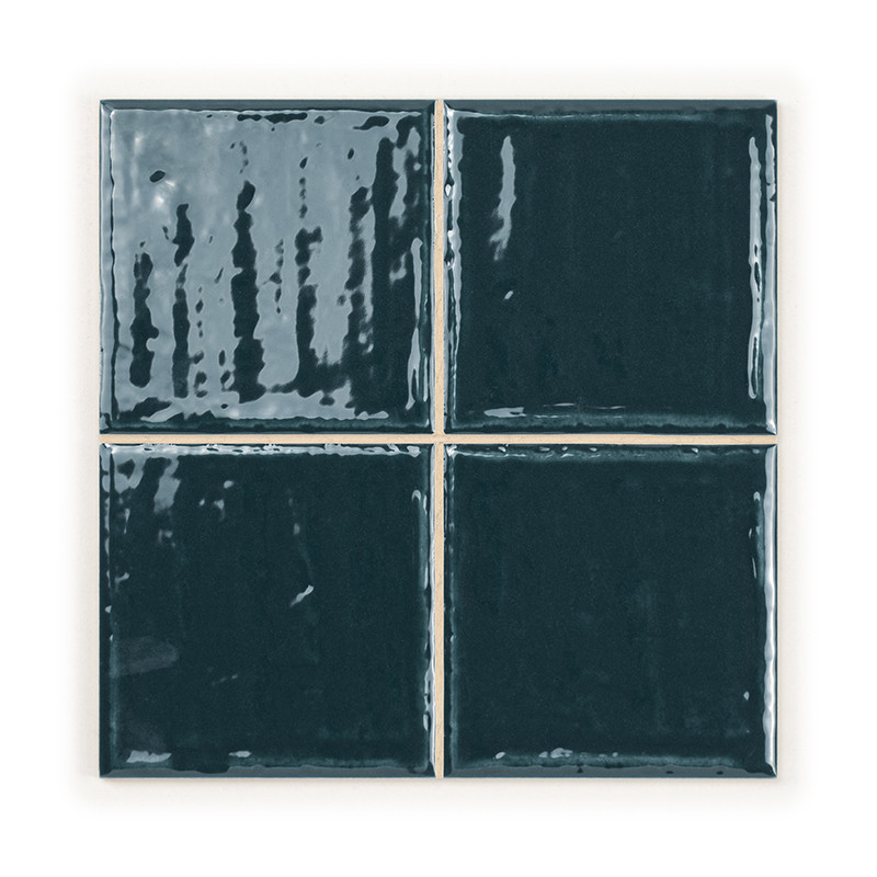 Quatre carreaux de céramique brillants vert foncé sont disposés en carré, réfléchissant la lumière et soulignant leur surface li