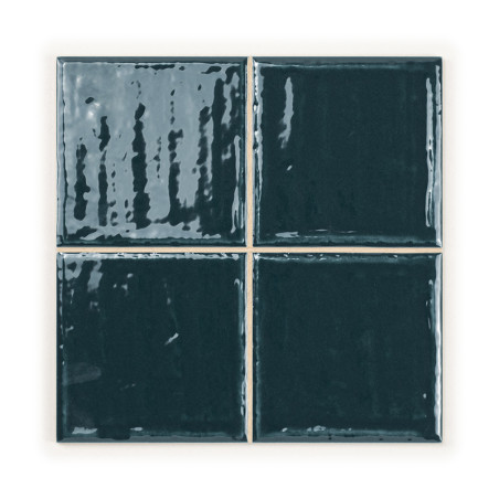 Quatre carreaux de céramique brillants vert foncé sont disposés en carré, réfléchissant la lumière et soulignant leur surface li