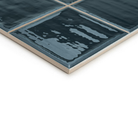 Un carreau de céramique bleu foncé brillant présente de légers motifs de vagues, disposés en grille, sur un fond blanc uni.