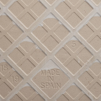 Un carreau de céramique beige avec un motif de grille en losange, avec le texte en relief « MADE IN SPAIN » au centre et des chi