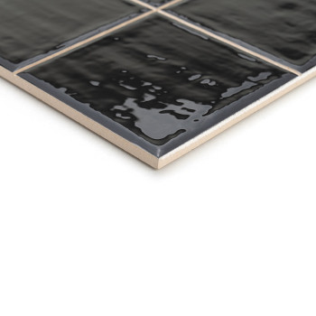 Un carreau de céramique noir brillant présente une surface texturée qui reflète subtilement la lumière. Il se trouve en biais su
