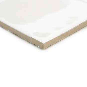 Een witte keramische tegel met een glanzende afwerking zit schuin en vertoont een beige, ongeglazuurde rand, wat een strak, mini
