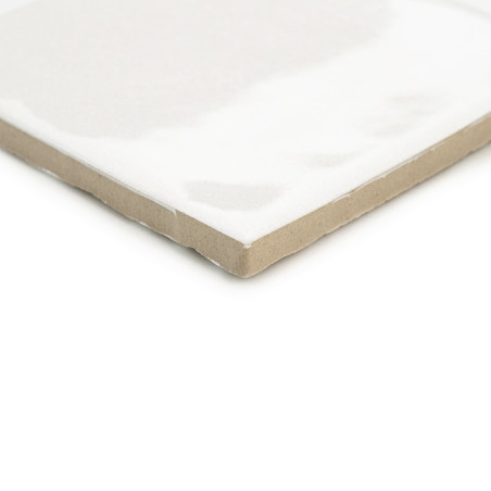 Eine weiße Keramikfliese mit glänzender Oberfläche liegt schräg und weist eine beige, unglasierte Kante auf, was ein klares, min