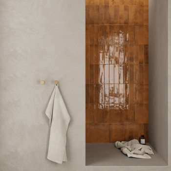 Un mur carrelé brillant de couleur brun rougeâtre forme un espace douche avec une serviette drapée sur un crochet sur un mur lis