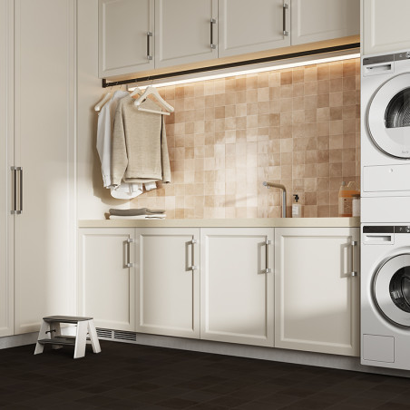 A laundry room features beige square tiles as a backsplash behind a sink, with white cabinets below. Clothes hang from a rod, an