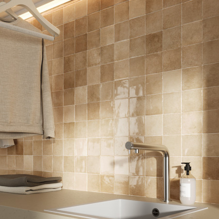 Beige ceramic tiles form a backsplash above a sink with a sleek faucet. Clothes hang neatly above, and a soap dispenser is nearb