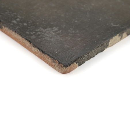 Een terracotta tegel met een donker, glad oppervlak ligt plat en vertoont afgebroken randen tegen een effen witte achtergrond.