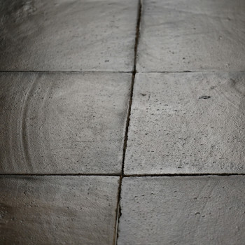 Aangrenzend liggen vierkante terracottategels, subtiel gestructureerd met cirkelvormige patronen, die bij weinig licht een verwe