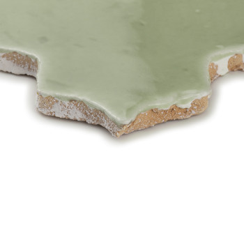 A green glazed terracotta tile sitting on a white surface, displaying rough, uneven edges and a rustic finish.