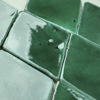 Ladrilhos de terracota verdes em forma de diamante dispostos em um padrão repetitivo, o esmalte refletivo captando a luz, criand