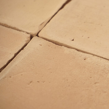 Os ladrilhos de terracota são dispostos em grade, formando uma superfície rústica em tons quentes sob luz natural.
