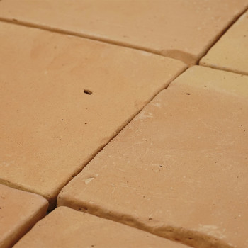 Terracottategels gerangschikt in een raster vormen een ruw, aards oppervlak, met kleine variaties in kleur en textuur.
