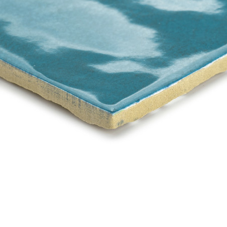 Un azulejo de cerámica muestra un patrón azul ondulado y brillante en su superficie, con un borde áspero de color beige claro, q