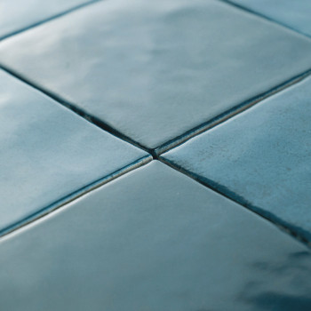 Cuatro azulejos azules lisos y brillantes se unen en las esquinas, creando un patrón de cuadrícula. La superficie es reflectante