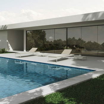 Una elegante piscina con agua azul emAzulejoda, flanqueada por tumbonas blancas, refleja una casa moderna con grandes ventanales