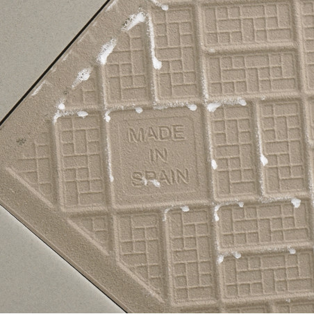 Un carreau de céramique beige présente un motif de grille avec le texte « MADE IN SPAIN » au centre, entouré de lignes de coulis