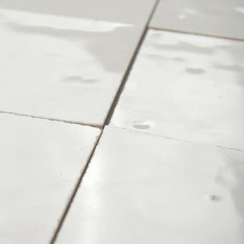 Azulejos de terracota blanca, brillantes y reflectantes, dispuestas en un elegante patrón de cuadrícula con líneas de lechada vi