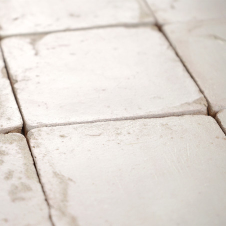 Les carreaux carrés en terre cuite sont disposés en grille, certains présentant une usure subtile, créant un aspect rustique au 