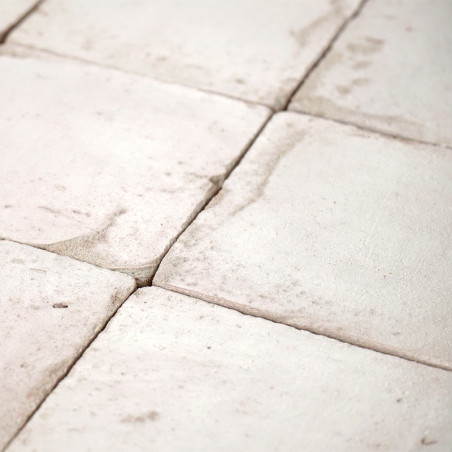 Les carreaux de terre cuite blanche, disposés en grille, présentent des variations de texture naturelles et des taches subtiles,