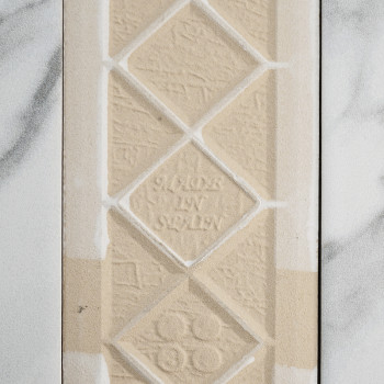 Op een beige tegel met textuur zijn diamantvormen in reliëf weergegeven met in het midden de tekst `MADE IN SWEDEN`. Het rust te