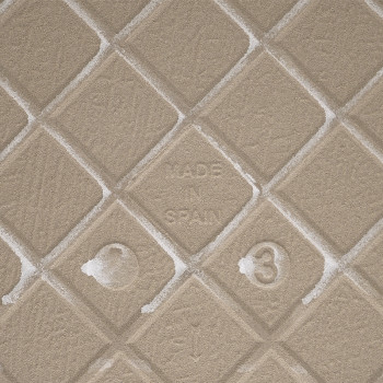 Um azulejo bege texturizado com um padrão de diamante em relevo exibe “MADE IN SPAIN” no centro, cercado por marcas de textura s