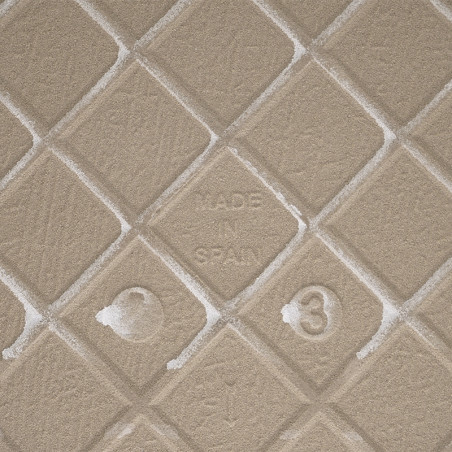 Un azulejo texturizado de color beige con un patrón de diamantes en relieve muestra `MADE IN SPAIN` en el centro, rodeado de sut Un azulejo texturizado de color beige con un patrón de diamantes en relieve muestra `MADE IN SPAIN` en el centro, rodeado de sut