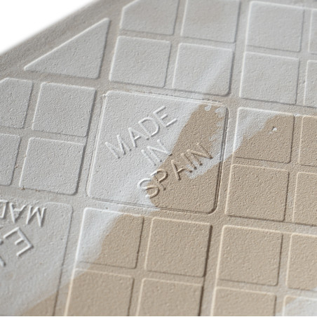 Un carreau beige pâle affiche le texte en relief « MADE IN SPAIN » au milieu d'un motif en grille, partiellement recouvert d'une