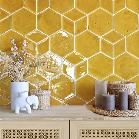 Sechseckige gelbe Terrakottafliesen bilden eine strukturierte Wand über einem Holztisch mit Kerzen und Dekorationsgegenständen.